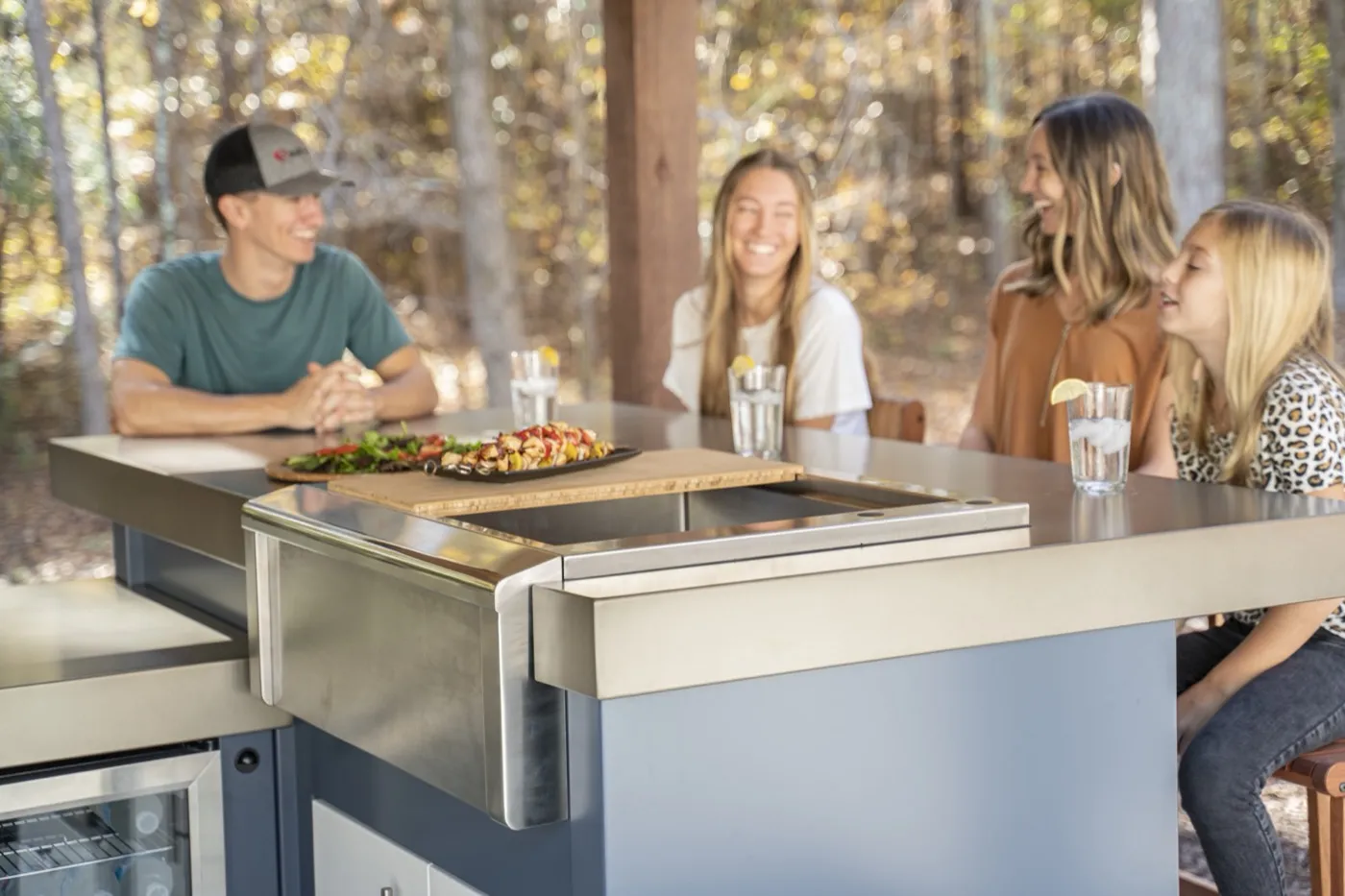 A Stoll outdoor kitchen island with a bamboo prep board, built-in griddle, and beverage fridge