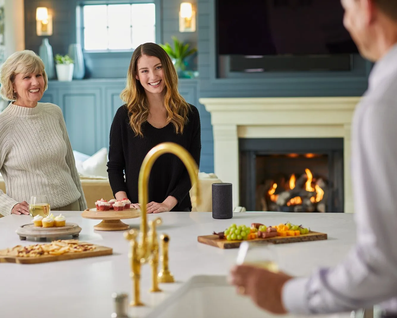 Three generations sharing snacks around a kitchen island with a gas fireplace burning in the room beyond