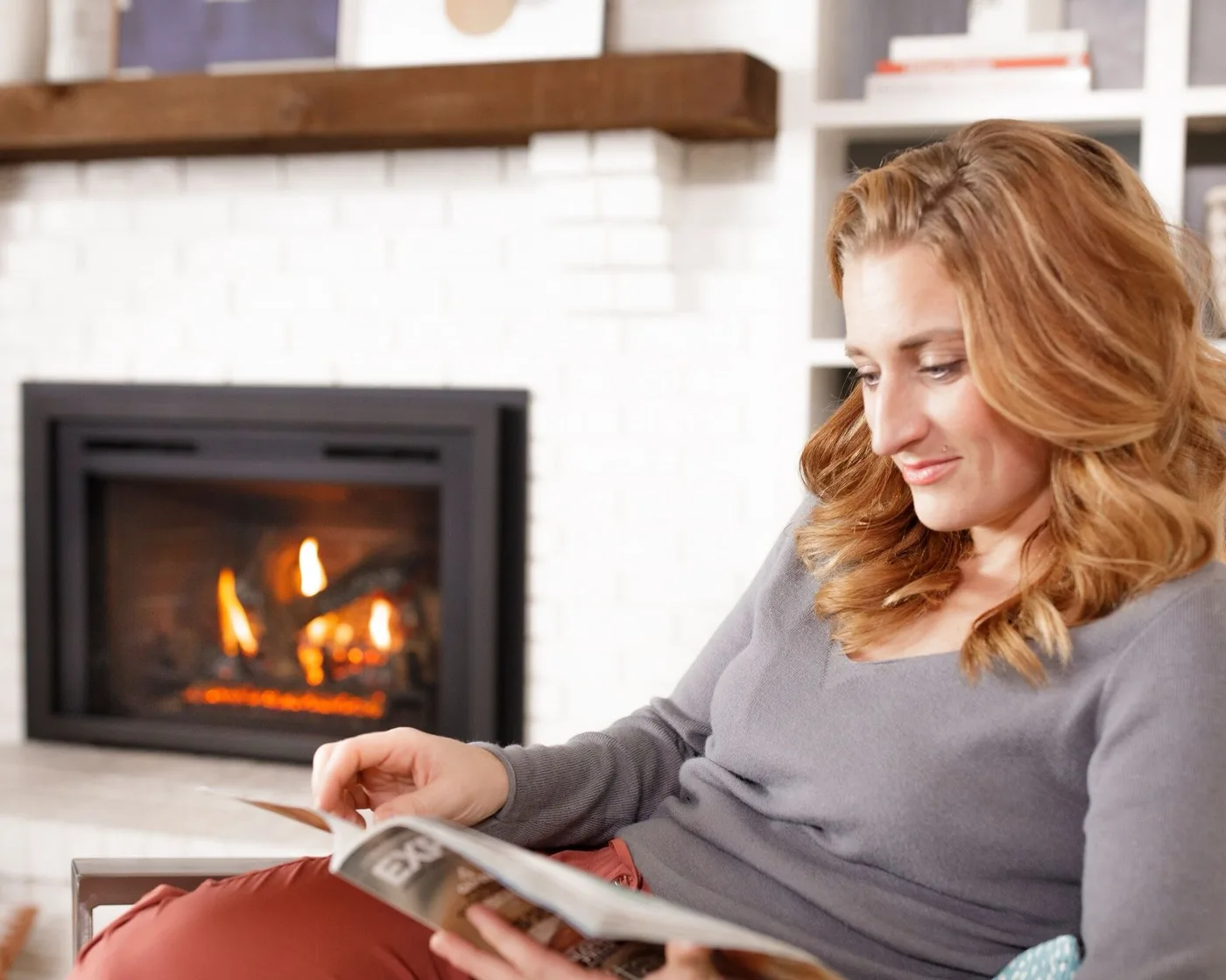 A woman reading beside a gas fireplace insert burning steadily in a bright living room