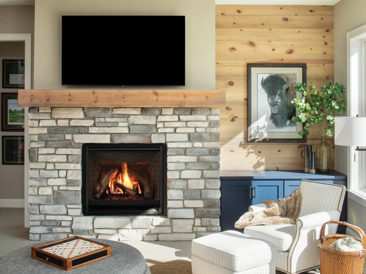 A timber mantel shelf over a stacked-stone fireplace surround with the fire burning below