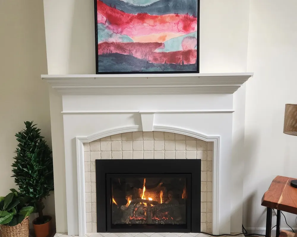 A finished gas insert with a white mantel and tile surround, lit