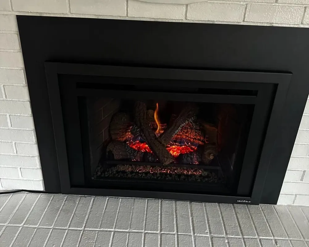 A black gas insert burning against white brick